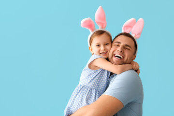 Happy young man with little daughter in Easter bunny ears on blue background