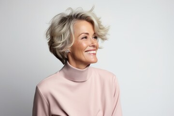 Portrait of a smiling senior woman in a pink sweater over grey background