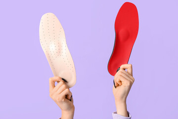 Female hands holding orthopedic insoles on lilac background
