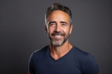 Portrait of a handsome middle-aged man smiling at the camera on a dark background - obrazy, fototapety, plakaty