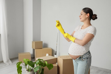 Young pregnant woman with rubber gloves preparing for cleaning in new apartment