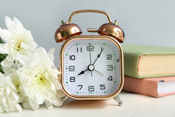 Alarm clock with chrysanthemum flowers and books on white wooden table