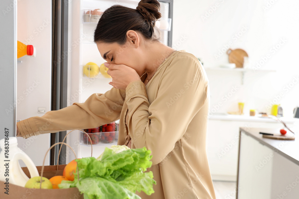 Poster Young pregnant woman feeling bad smell from fridge in kitchen