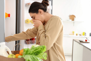 Young pregnant woman feeling bad smell from fridge in kitchen