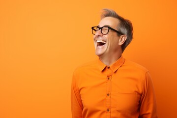 Portrait of a happy senior man in orange shirt and glasses over orange background.