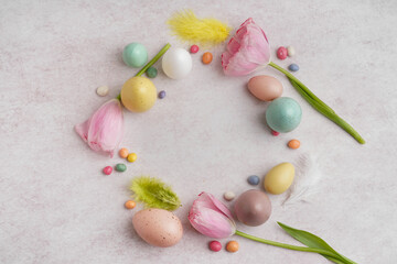 Easter wreath made of tulips, color eggs, candies and feathers on light background