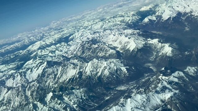 Aerial view, pilot POV of the snowed Alps mountain range, shot from the cockpit of an arplane during a right turn. Sunny daylight with a blue sky. 4K