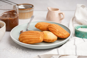 Plate with tasty madeleines and spoon on table near light wall