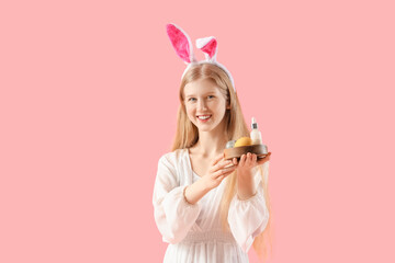 Beautiful young woman in bunny ears holding board with Easter eggs and essential oil on pink background