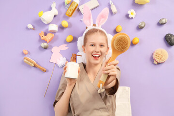 Happy female massage therapist with Easter decor and spa supplies lying on color background