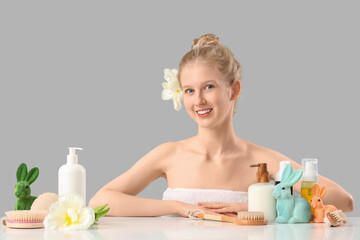 Obraz na płótnie Canvas Beautiful young woman with spa supplies and Easter bunnies at table against grey background