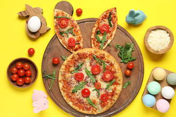Easter pizza with bunny ears, painted eggs and tomatoes on yellow background