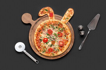 Easter pizza with bunny ears, eggs, spatula and pizza cutter on black background