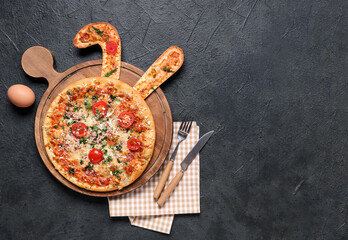 Tasty Easter pizza with bunny ears, egg and cutlery on black background
