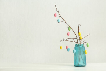 Tree branches with Easter eggs in blue glass vase on white background