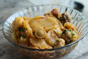 Seblak is a typical Indonesian dish with a savory and spicy taste. cooked with vegetables, sausage, eggs, chicken feet, seafood and processed beef. a bowl of seblak on a wooden table.