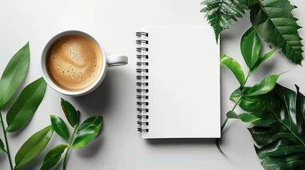 Fotobehang Blank white spiral notebook on table surrounded by coffee and green leaves, in flat lay photography style with minimalist aesthetic, taken from top view perspective on white background. © Surachetsh