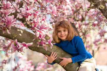 Little kid smelling spring flower outdoor. Portrait of smiling child face near blossom spring flowers. Kid among branches of spring tree in blossoms. Cute kids face surrounded by spring blossom