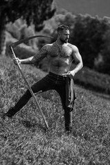Strong muscular power sexy farmer using scythe. Farmer with a scythe on green grass field. Guy cut...