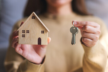 Closeup image of a woman holding a wooden house model and the keys for real estate concept