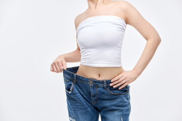 A young, slim Asian woman is checking her diet success by wearing jeans in sizes larger than her...