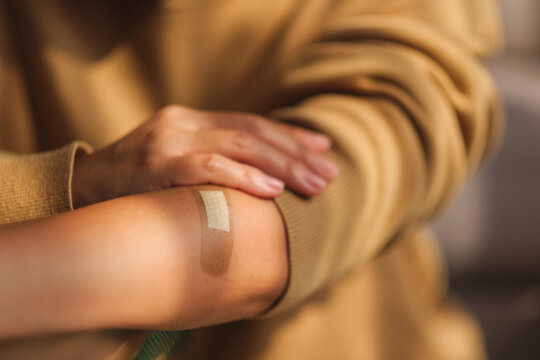 Closeup image of a young woman pointing finger at a adhesive bandage, medical plaster, band aid on her arm
