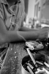 Burnt cigarette in an ashtray with a women on the background sitting while holding handphone in a...