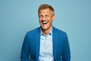 Portrait of a happy mature man laughing and looking at camera over blue background