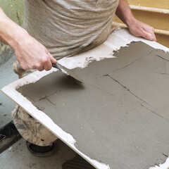 A construction worker applies cement to ceramic tile with a spatula