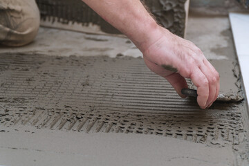Construction worker applies cement for laying floor ceramic tiles with spatula
