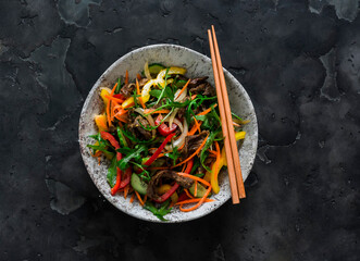 Warm salad with beef, sweet pepper, arugula on a dark background, top view