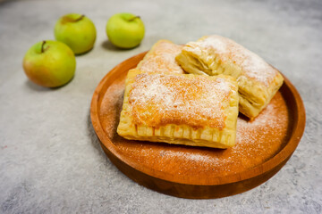 Homemade mini apple pie pastry placed on a plate with fresh apple in the background