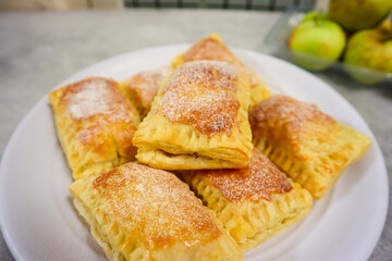 Homemade mini apple pie pastry placed on a plate with fresh apple in the background