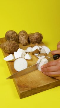woman hands with knife cutting eddo into cubes on wooden board on yellow background