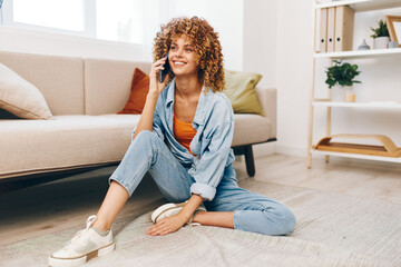 Happy young woman holding mobile phone while relaxing on cozy sofa at home