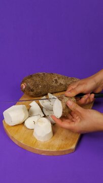woman hands with knife cutting malanga into cubes on wooden board on purple background