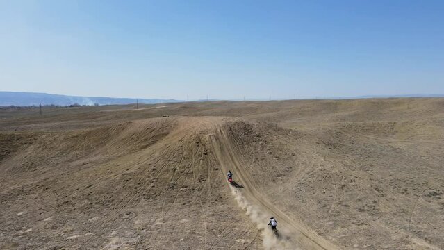 An action-packed, 4K drone shot of two motocross riders hitting a big hill jump, in the desert-like terrain of Grand Valley OHV area, located in Grand Junction, Colorado.