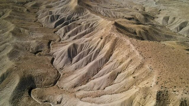 A spectacular 4K drone shot over the barren, desert hills of Grand Valley OHV area, with the steep-sloped plateaus of the Little Book Cliffs in the distance, located in Grand Junction, Colorado.
