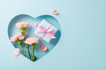 Mother's Day sophisticated display, from top view, featuring carnations, a gift wrapped in silk, paper hearts, all visible through heart-shaped hole on pastel blue background, with empty space - obrazy, fototapety, plakaty