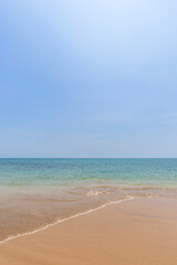 Front view of a small wave crashing on a sandy beach, sea and blue sky on a sunny day. Natural tropical travel and vacation background with copy space.