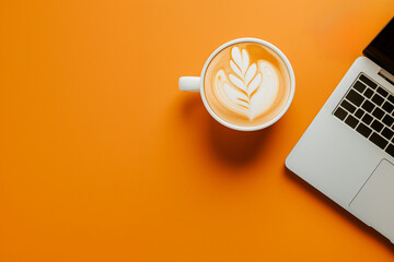 tasse à café blanche remplie d'un art caffe latte à la mousse blanche, à côté d'un ordinateur portable ouvert, laptop et café sur un fond orange espace négatif copy space - obrazy, fototapety, plakaty
