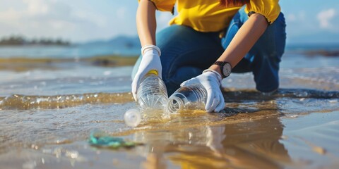 close-up of volunteer with gloves picking up a plastic bottle in the beach  - obrazy, fototapety, plakaty