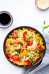 Spicy stir fry noodles with shrimps, colorful paprika, green pea, green onion and sesame seeds with ginger, garlic and soy sauce. White table background, top view