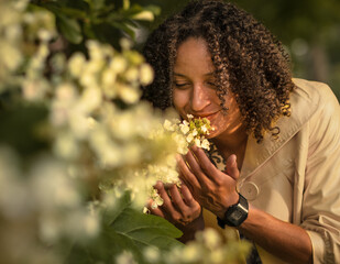 Outdoor portrait of Attractive African-American young woman smelling blooming flowers in summer