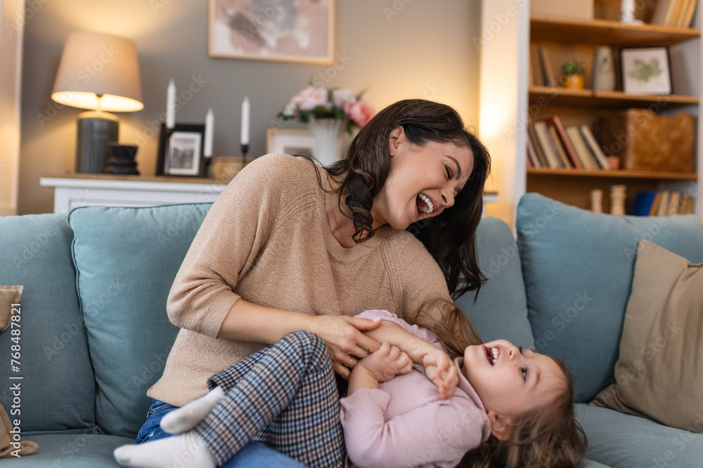 Wall mural Happy mama with girl child, hug in home and weekend play time lifestyle for mom parent. Funny crazy kid in living room, mother holding toddler with smile and love bonding together on mothers day