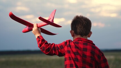 Cheerful male kid running with red airplane toy imagine pilot flight at summer field closeup back...
