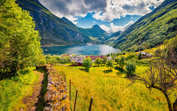 Wonderful summer view of green meadow in Geiranger village with huge peak on background, western Norway, Europe. Picturesque morning scene of Sunnylvsfjorden fjord. Traveling concept background.