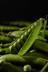 Open pod of young green peas with round peas close-up,Indoor black background and wooden bowl