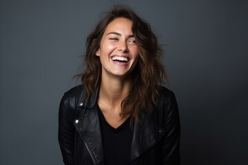 Obraz na płótnie Canvas Portrait of a laughing young woman in leather jacket over grey background