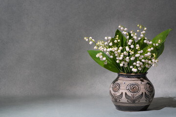 A small bouquet of fresh spring flowers. Lilies of the valley in a light vase isolated on a gray...